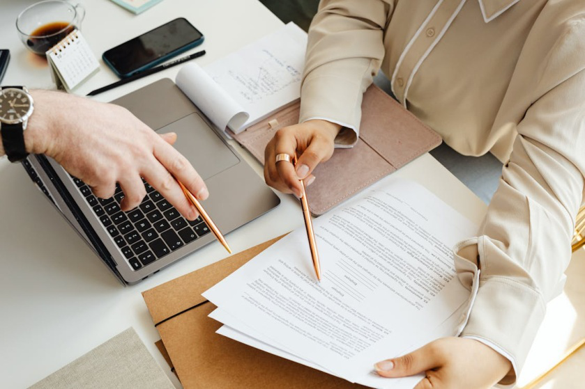 An image of two people pointing at documents with their pens