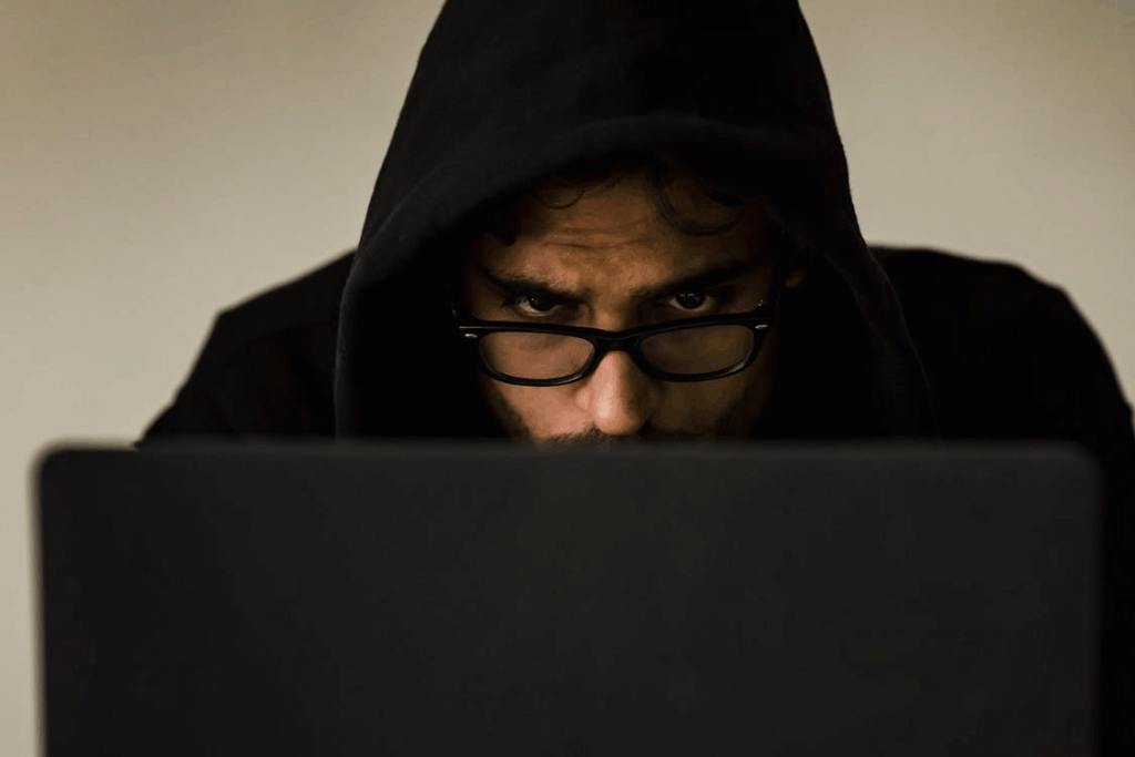 Hooded individual using a laptop, representing online accusations and digital age fraud cases in Mississauga