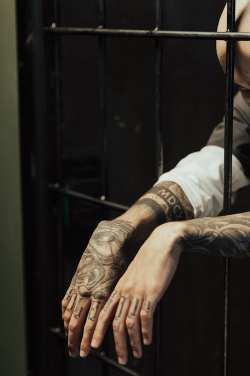 Prisoner’s tattooed hands clasped together behind bars, highlighting the serious consequences of white-collar crime convictions