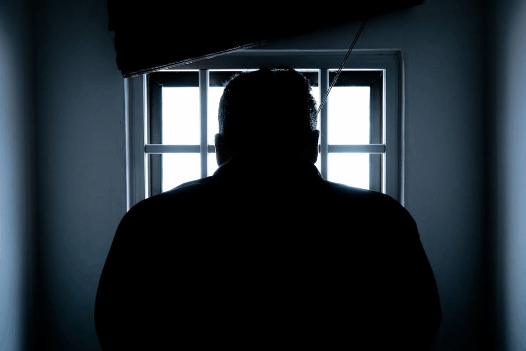 Silhouette of a man standing by a window, reflecting on his upcoming domestic assault court case